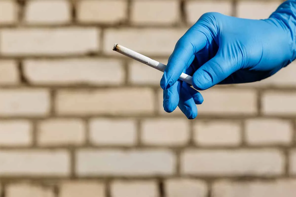 a hand in a blue medical glove holding a lit cigarette